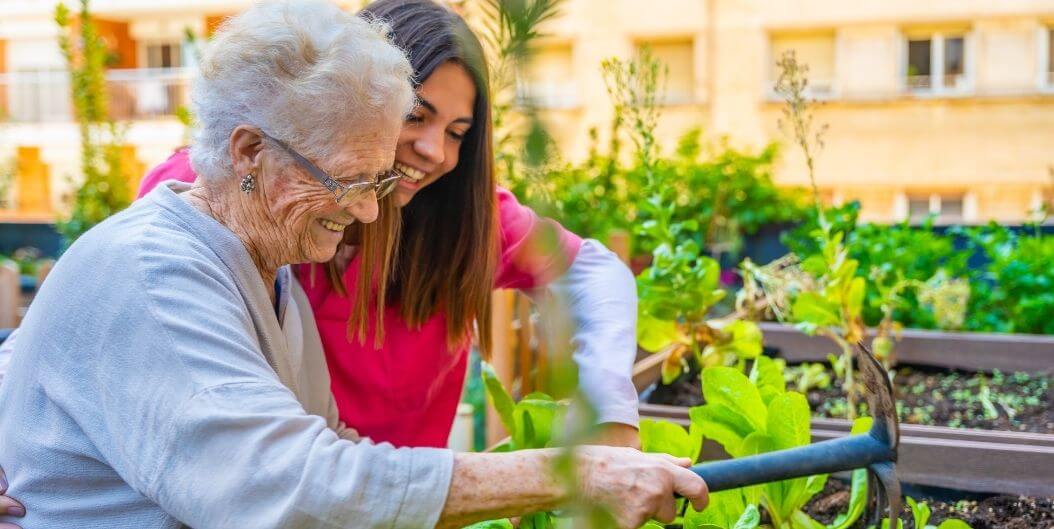 Elderly Woman Gardening with Caregiver in Lush Garden at Independent Living Facility