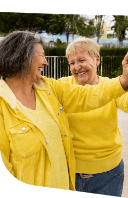 Two Elderly Women in Yellow Dancing Joyfully Outdoors at an Independent Living Community
