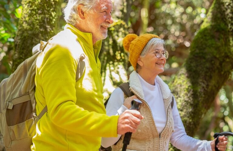 Elderly Couple Hiking Through a Lush Forest With Trekking Poles Near an Independent Living Facility