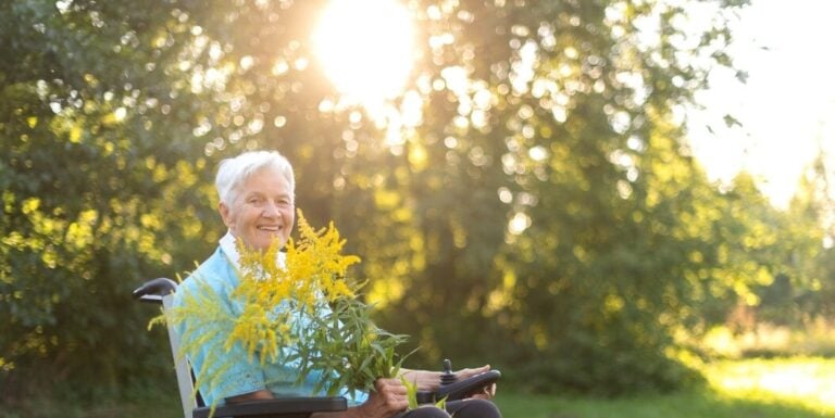Smiling Elderly Woman Enjoying Sunshine and Flowers Outdoors at Independent Living Facility